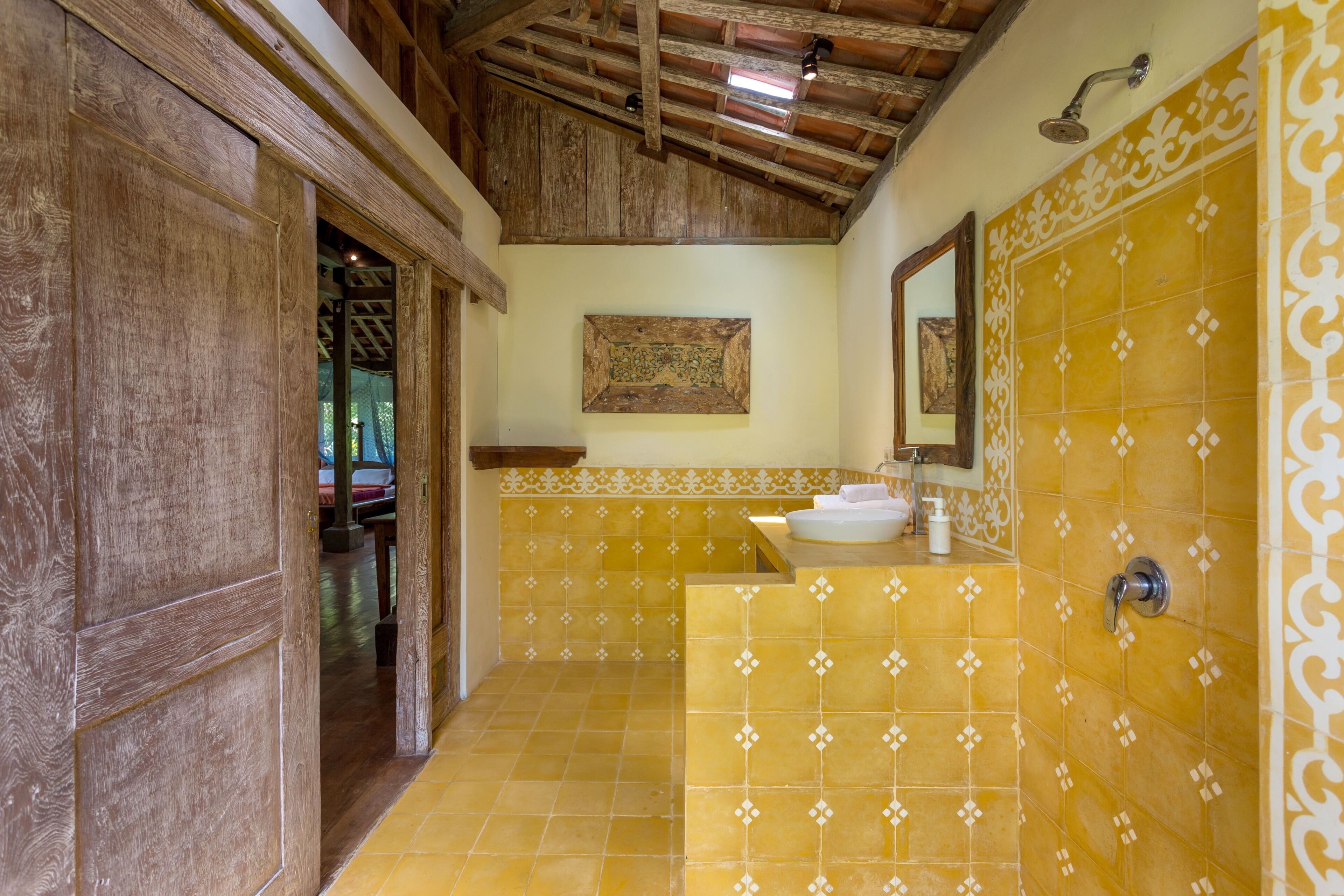 Un baño con vigas de madera, un lavamanos y azulejos estampados amarillos.