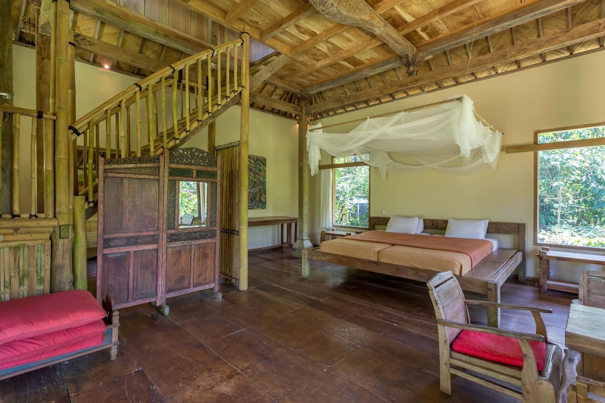 Ein geräumiges Zimmer mit einer Holztreppe, einem großen Bett mit Baldachin und Blick auf die grüne Umgebung.