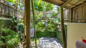A covered outdoor area with a wooden deck, surrounded by lush greenery and a bamboo structure.