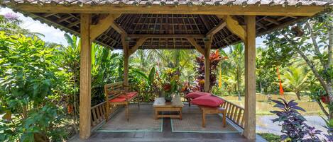 A wooden gazebo with a tiled roof, surrounded by lush greenery and tropical plants.