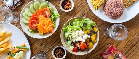 A variety of dishes on a wooden table, including salads, rice, and vegetables.