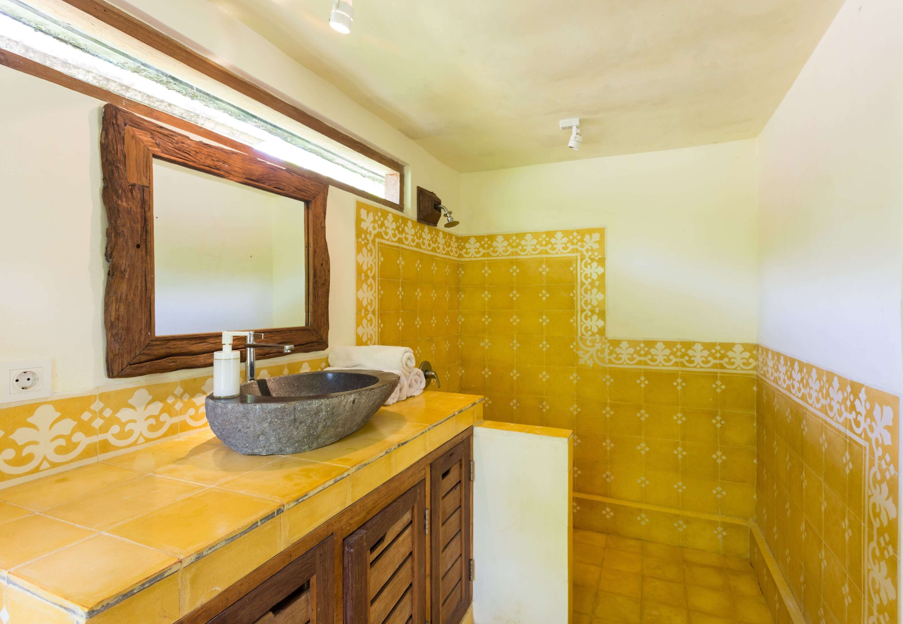 Un baño con lavamanos de piedra, armarios de madera, un espejo y baldosas amarillas con estampado.