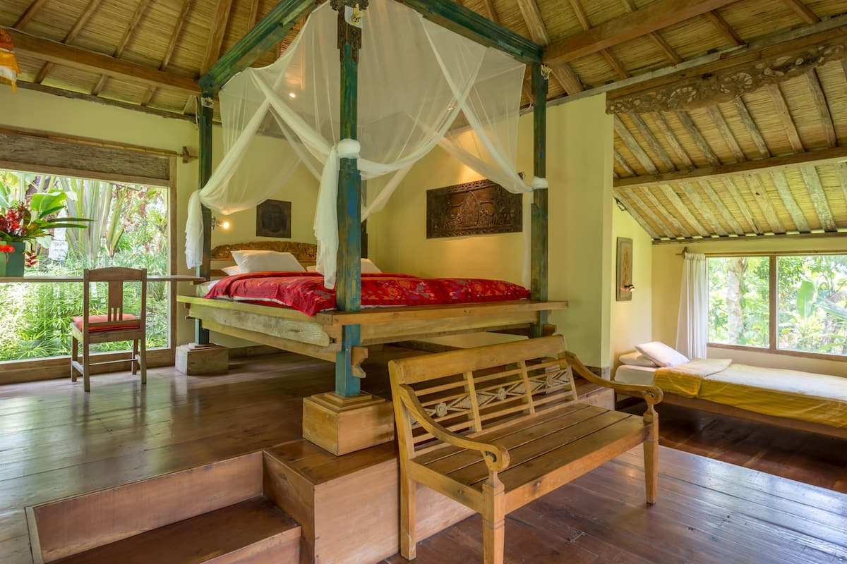 Ein Zimmer mit einem Himmelsbett, einer Bank und einem Sessel.