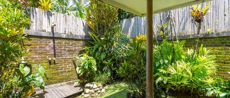 A garden with a wooden deck, a brick wall, and various tropical plants.