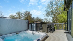 A hot tub on a wooden deck with a view of trees and a building in the background. - 1 bedroom accommodation in Bewaldeth, Keswick (Bewaldeth, Keswick)