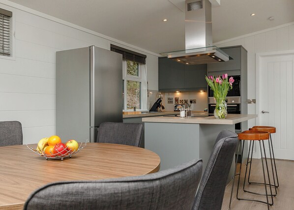 A modern kitchen with a central island, a dining area with a wooden table and grey chairs, and a vase with flowers on the island.
