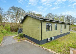 Ein eingeschossiges Gebäude mit grüner Fassade, einer kleinen Veranda und einem gepflasterten Einfahrt.