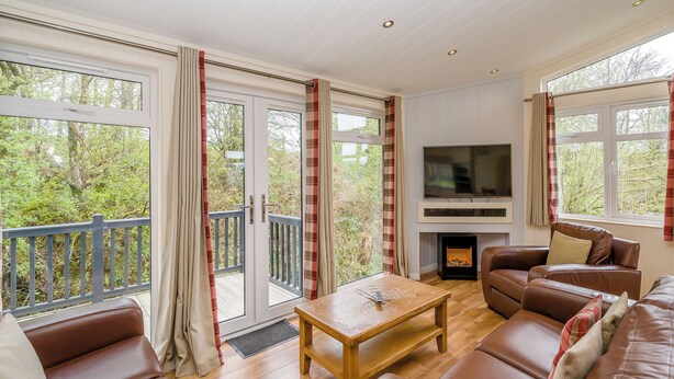 Una sala de estar acogedora con chimenea, sofás de cuero, una mesa de centro y ventanas grandes con cortinas.
