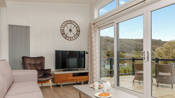 A modern living room with a flat-screen TV, comfortable seating, a dining area with a table, and a large window with a view of the outdoors. - 4 bedroom accommodation in Cheddar (Cheddar)
