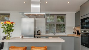 A modern kitchen with a central island, stainless steel appliances, and a window with blinds. - 4 bedroom accommodation in Cheddar (Cheddar)