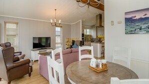 A living room with a TV, sofa, chairs, a dining table with a tray, and a kitchen in the background. - 1 bedroom accommodation in Bewaldeth, Keswick (Bewaldeth, Keswick)