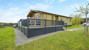 A single-story mobile home with a deck, a covered outdoor seating area, and a gravel driveway. - 1 bedroom accommodation in Bewaldeth, Keswick (Bewaldeth, Keswick)