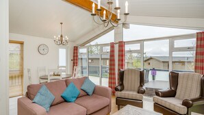 A cozy living room with a sofa, armchairs, a chandelier, a dining table, and a large window with curtains. - 1 bedroom accommodation in Bewaldeth, Keswick (Bewaldeth, Keswick)