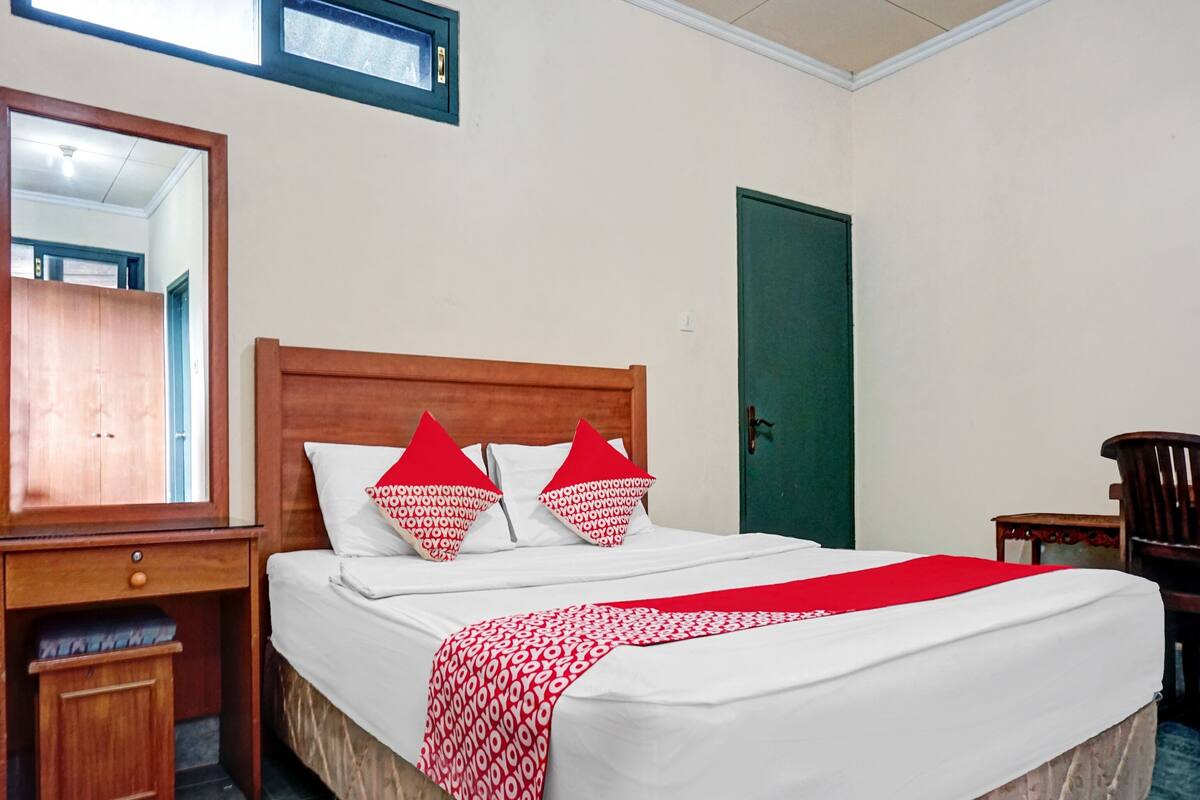 A hotel room with a wooden bed, a nightstand, a mirror, a green door, and a small table.