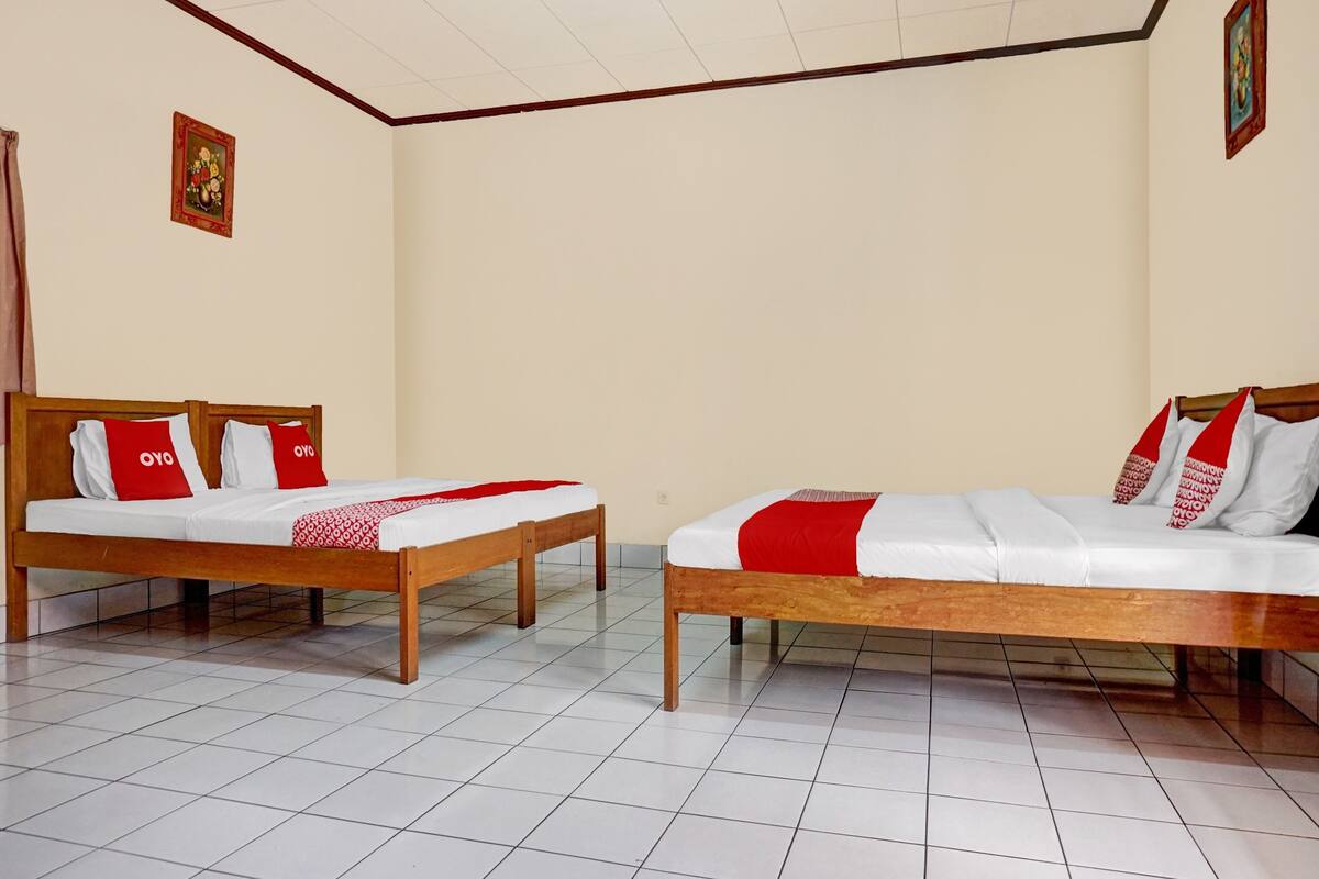 A hotel room with two wooden beds, white bedding, and red pillows with "OYO" text.