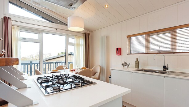 Une cuisine moderne équipée d’une cuisinière à gaz, de meubles blancs et d’une fenêtre avec des stores, ainsi que d’un balcon visible à travers la fenêtre.