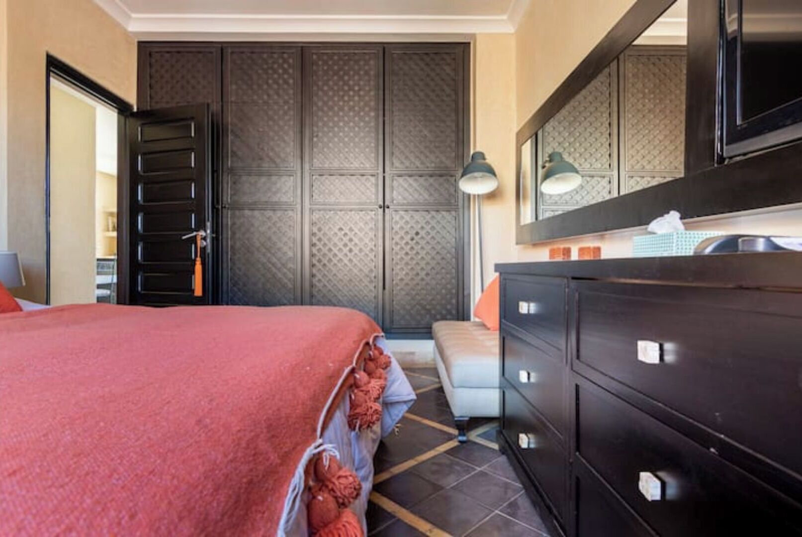A hotel room with a bed, a dresser, a mirror, and a door with a patterned design.