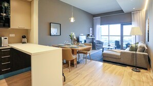 Una sala de estar moderna con un sofá, un comedor con una mesa preparada para cuatro personas y una zona de cocina con microondas y cafetera.