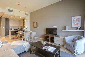 Un salon moderne avec un canapé, une table basse, un téléviseur et un coin repas comprenant des chaises, et une cuisine en arrière-plan.