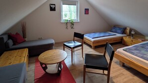 Een gezellig slaapkamer op zolder met een schuine plafond, een raam met uitzicht, een houten vloer, een bank, een bed, een stoel en een kleine tafel.