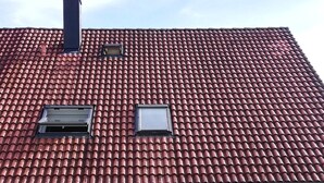 Een gebouw met een rode dakbedekking, een dubbele deuropening en een kleine tuin met bloemen.