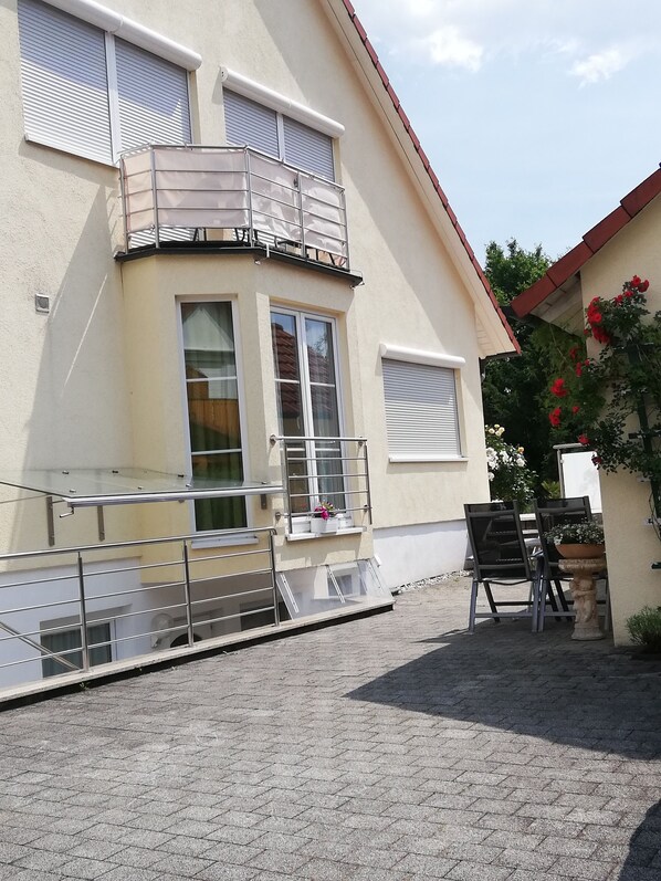 A building with a balcony, a window with a view, and a paved courtyard.
