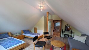 Een knus zolderkamer met een bed, bureau, stoel, slaapbank en een boekenkast.