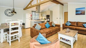 A spacious living area with a wooden ceiling, a dining table with chairs, a brown sofa with blue cushions, and a kitchen in the background. - 4 bedroom accommodation in Bewaldeth, Keswick (Bewaldeth, Keswick)
