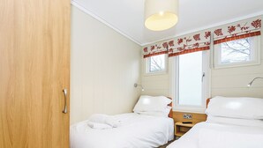 A room with two beds, a wooden wardrobe, a window with curtains, and a bedside table with a lamp. - 4 bedroom accommodation in Bewaldeth, Keswick (Bewaldeth, Keswick)