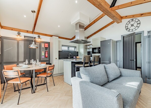 Una cocina moderna con una isla central, zona de comedor con sillas anaranjadas y un sofá gris.