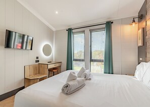 Habitación de hotel con cama, escritorio, espejo, televisor y ventana con cortinas.