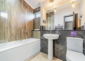 Un baño moderno con pared de madera, una bañera blanca, un lavamanos y un inodoro.