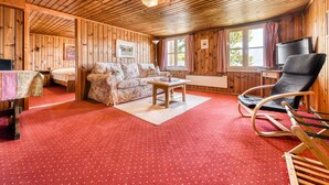 A wooden cabin interior with a red carpet, a sofa, a rocking chair, and a table. - Berghaus Tschengla (Buerserberg)