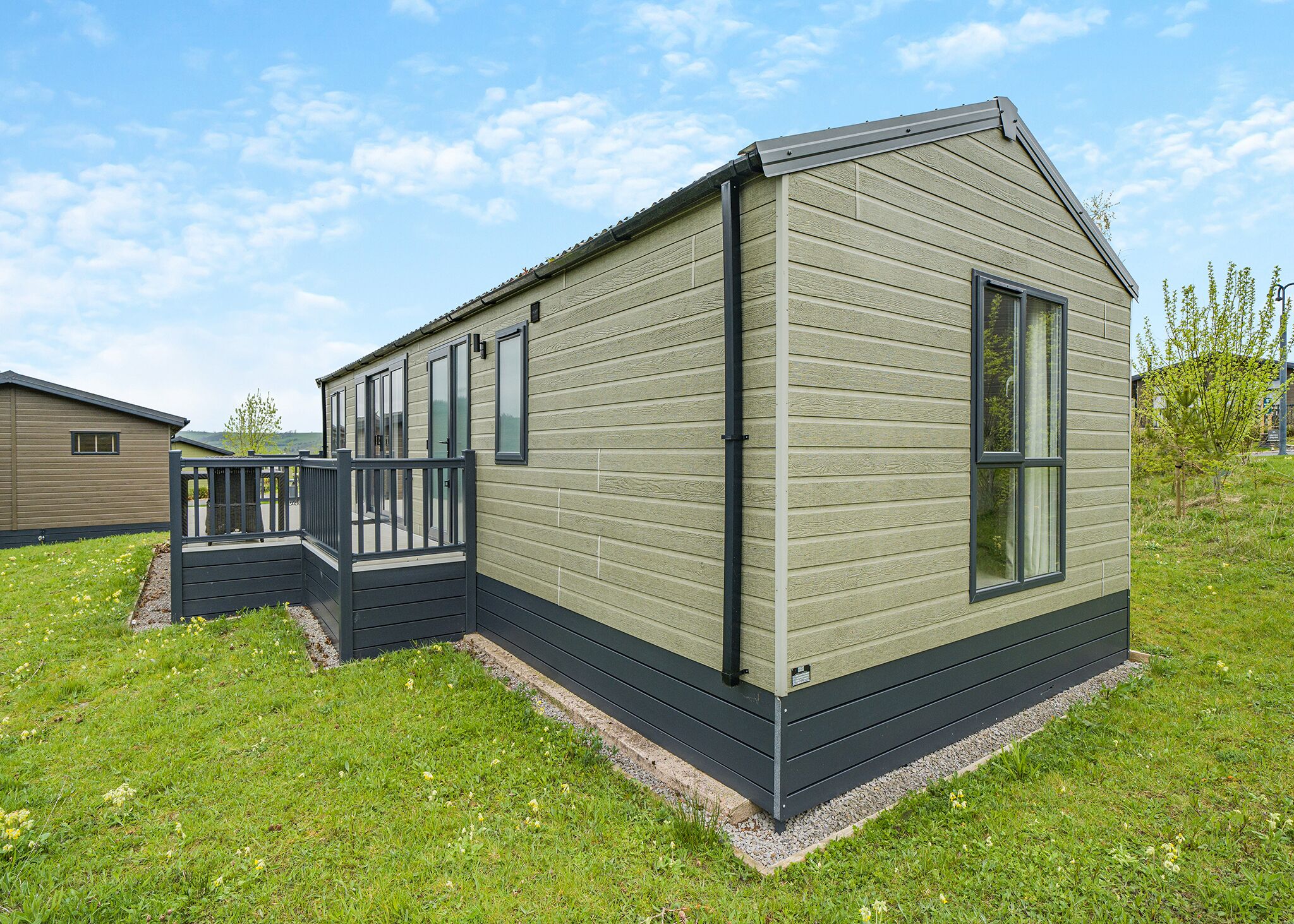A single-story mobile home with a deck, large windows, and a sloped roof.