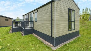 Une maison mobile de plain-pied dotée d’une terrasse, de grandes fenêtres et d’un toit en pente.