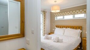A bedroom with a wooden bed, white bedding, a bedside table, a mirror, and a window with a patterned curtain. - 2 bedroom accommodation in Bewaldeth, Keswick (Bewaldeth, Keswick)