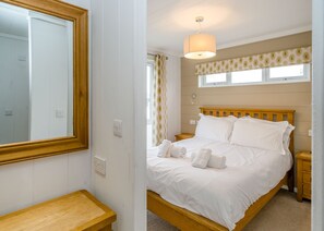 Ein Schlafzimmer mit einem hölzernen Bett, weißer Bettwäsche, einem Nachttisch, einem Spiegel und einem Fenster mit einem gemusterten Vorhang.