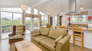 A cozy living room with a sofa, armchair, and dining table, a kitchen with a stove and refrigerator, and large windows offering a view of the outdoors. - 2 bedroom accommodation in Bewaldeth, Keswick (Bewaldeth, Keswick)