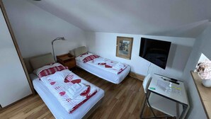 A small, tidy room with two single beds, a desk, a chair, a TV, and a framed picture on the wall. - Small apartment for a maximum of 2 people in a unique location directly on the lake (Rottach-Egern)