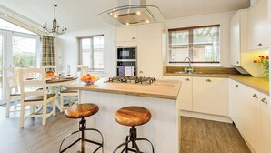 A modern kitchen with white cabinetry, a central island with stools, a built-in microwave, and a large window with blinds. - 1 bedroom accommodation in Holton Heath (Holton Heath)