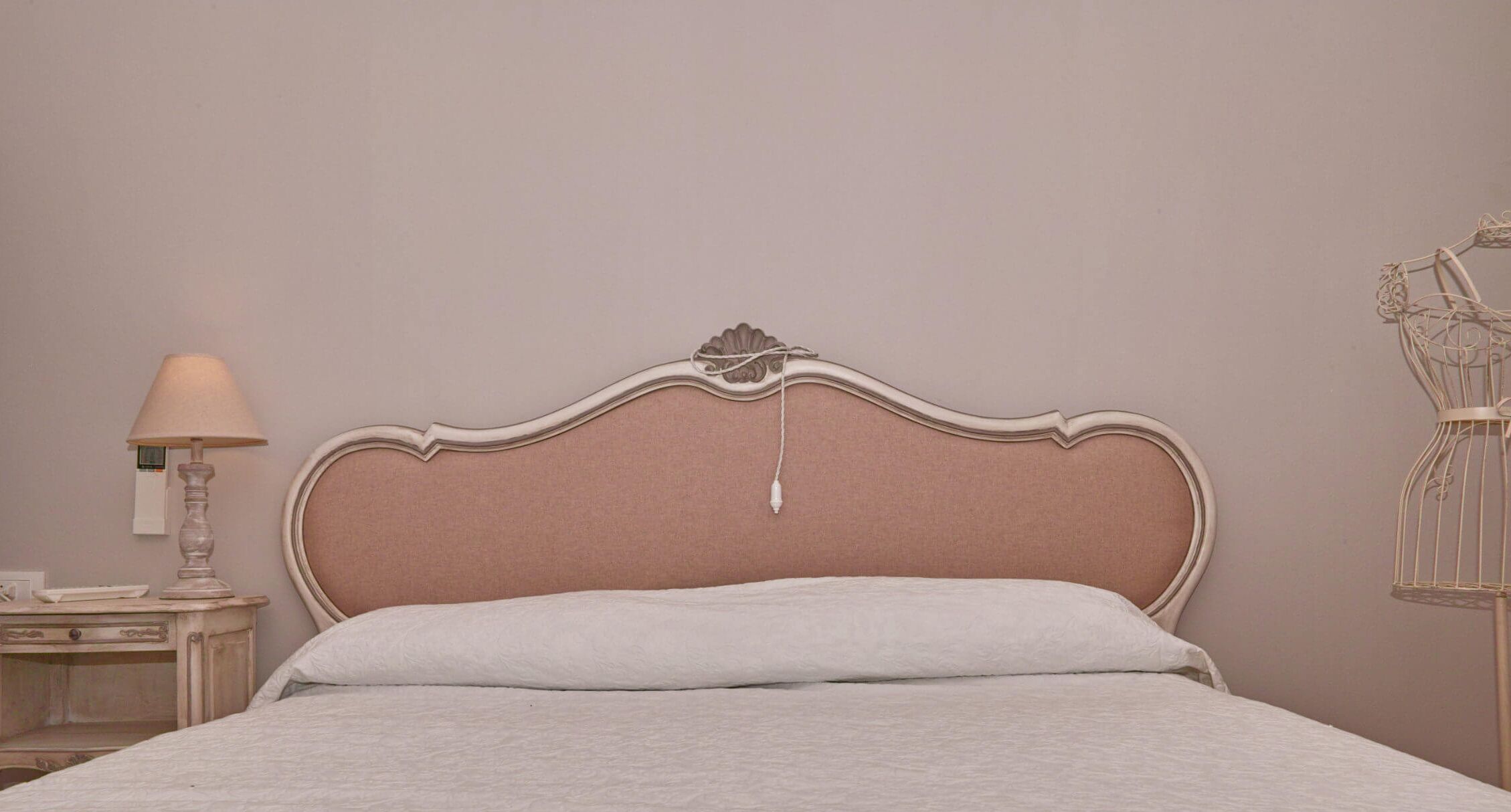 A neatly made bed with a headboard, a bedside lamp, and a nightstand with a lamp.