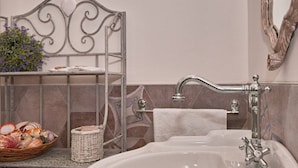 Une salle de bain avec un étagère en métal sur laquelle repose un panier rempli de coquillages, un lavabo blanc et un miroir décoratif.