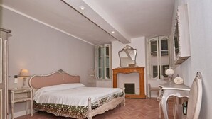 Une chambre à coucher avec un lit, une coiffeuse avec un miroir, une cheminée et une fenêtre avec des volets.