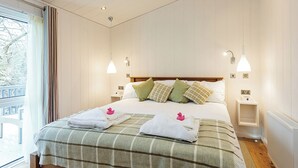 A hotel room with a bed, two bedside tables, a window with curtains, and a view of trees outside. - 3 bedroom accommodation in Wootton Bridge, Nr Cowes (Wootton Bridge, Nr Cowes)