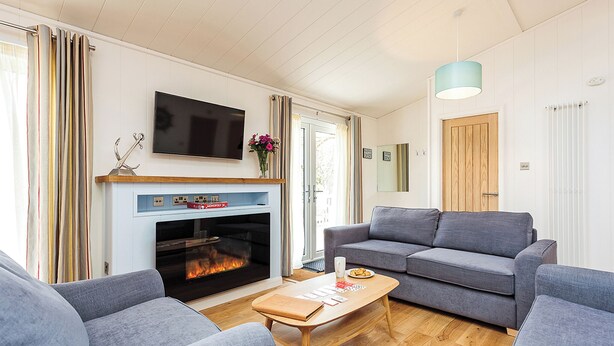 A living room with a fireplace, grey sofas, a wooden coffee table, and a TV mounted above the fireplace. - 3 bedroom accommodation in Wootton Bridge, Nr Cowes (Wootton Bridge, Nr Cowes)