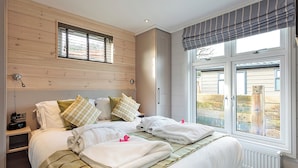 Une chambre à coucher avec une tête de lit en bois, un lit recouvert de draps blancs, une table de chevet avec une horloge et une fenêtre donnant sur l’extérieur.