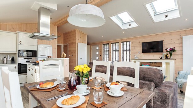 Une cuisine moderne avec des appareils électroménagers blancs, une table à manger avec une vaisselle assortie et un coin salon confortable avec un canapé marron.