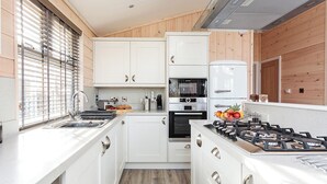 Une cuisine compacte avec des meubles blancs, un four encastré, une cuisinière à gaz et une fenêtre équipée de stores.