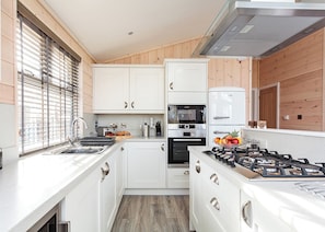 Una cocina compacta con armarios blancos, horno empotrado, estufa a gas y ventana con persianas.