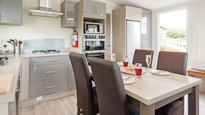 Eine moderne Küche mit Essbereich, inklusive Tisch mit Stühlen, Gasherd, Backofen, Mikrowelle und Blick ins Freie.